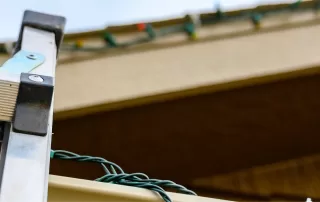 a ladder rests against the roofline of home with a set of colorful christmas lights to celebrate the holiday season