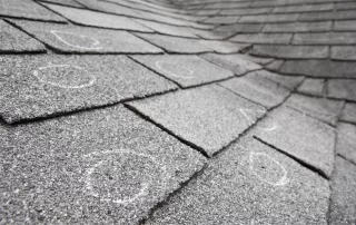 Old roof with hail damaged shingles, chalk circles mark the damage. Shallow depth of field