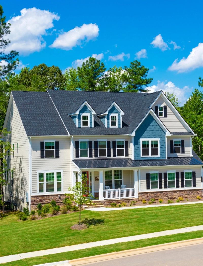 A beautiful blue house against a cloudy blue sky and greenery.