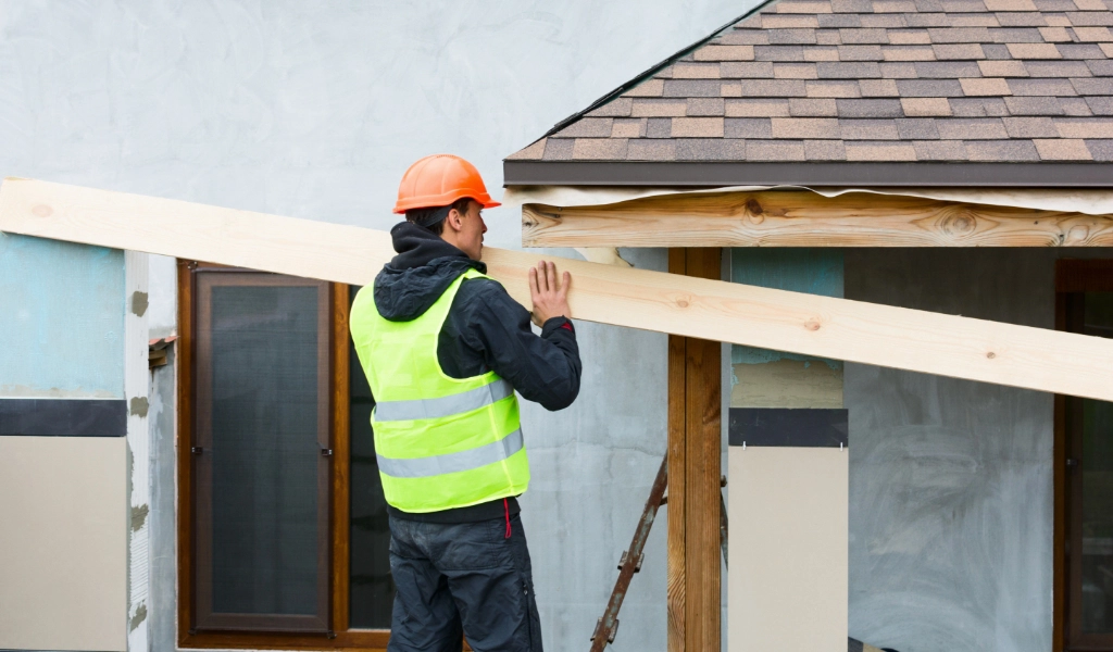 A man in a safety vest and hard hat holds a wooden beam while working on a home restoration project.