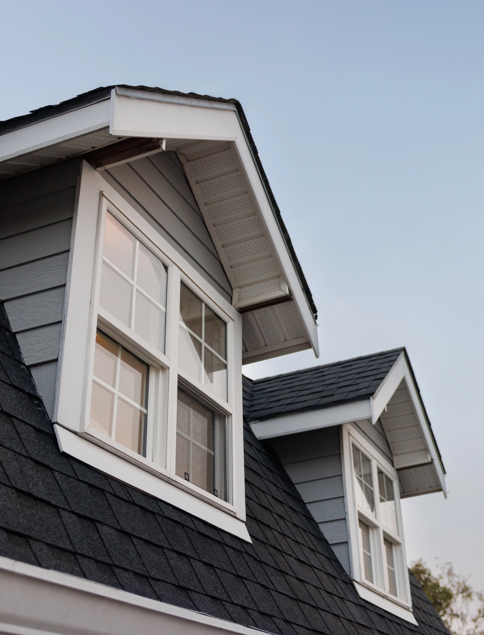 Two windows coming out of a residential shingle roof.