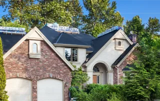 Residential home with roofing materials stacked on the roof, indicating a roof replacement in progress during clear weather.