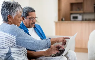 Smiling couple sitting together at home using a laptop, reviewing and filing a home insurance claim online.