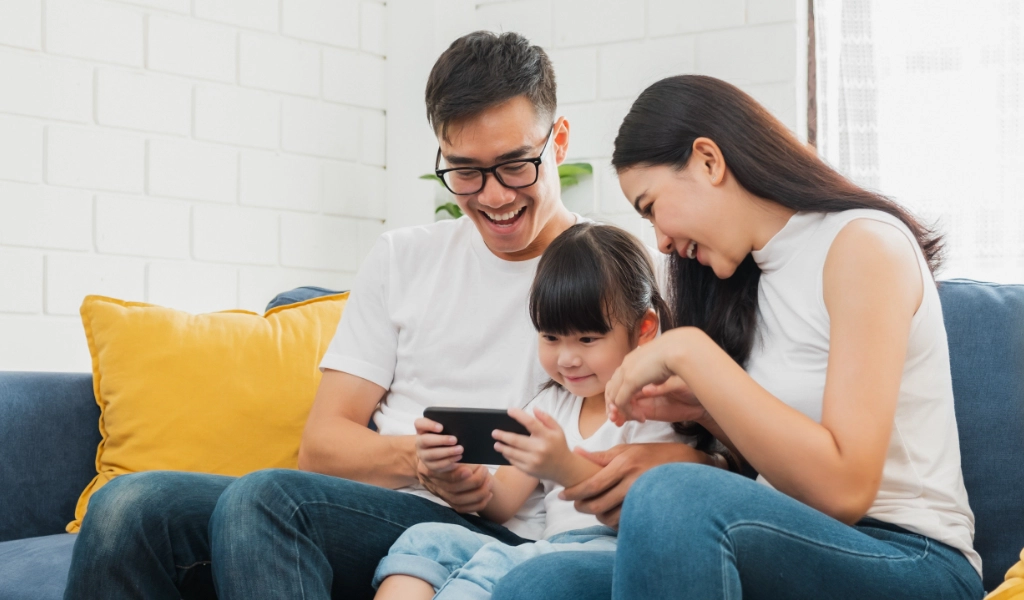 A family sits on the couch and looks at a phone.