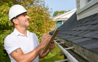 A roofer in a hard hat inspects a home's roof.