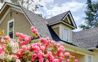 A new roof on a home with pink flowers in the foreground.